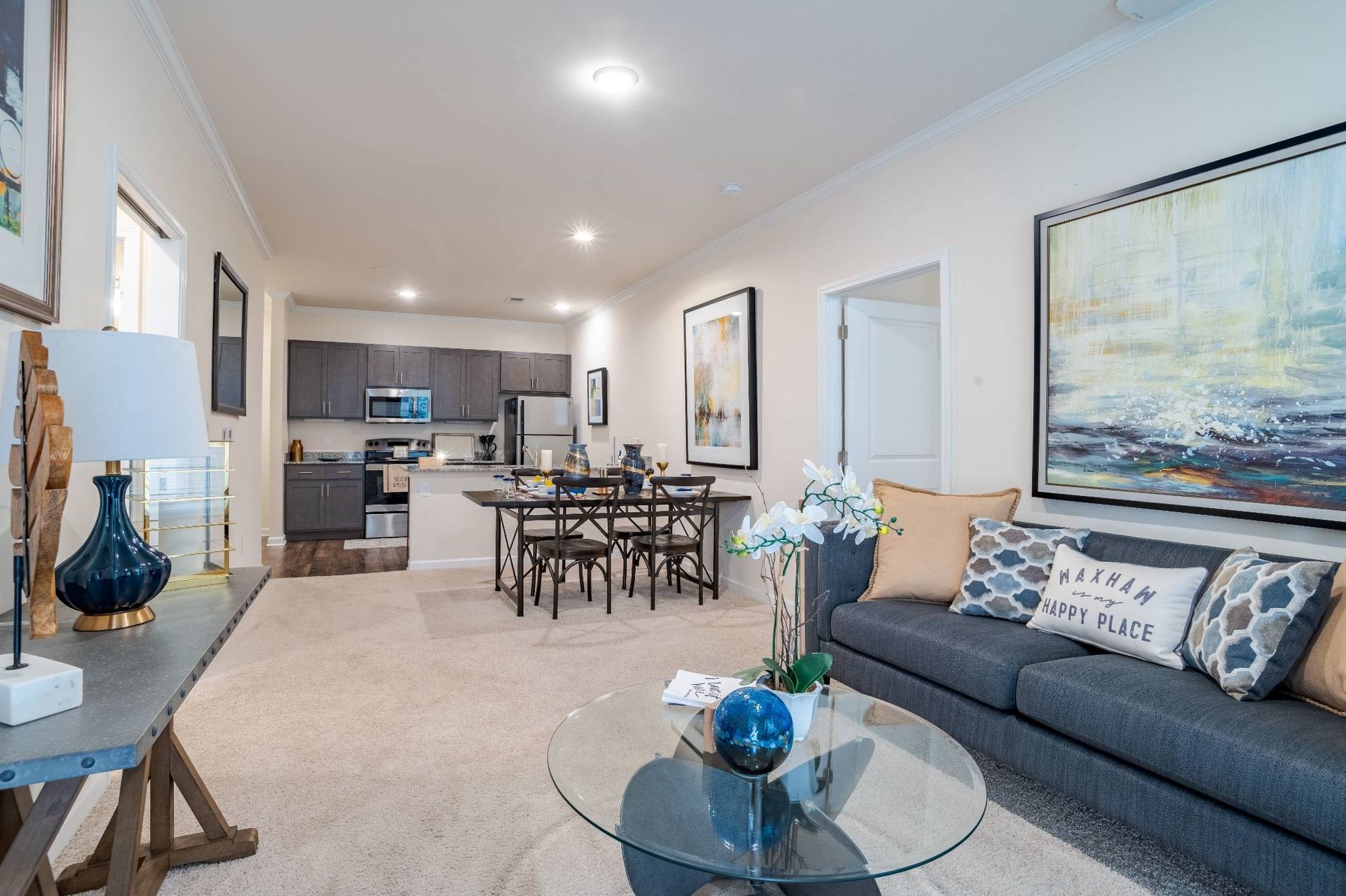 Open-concept living room with sofa, glass coffee table, and visible kitchen.
