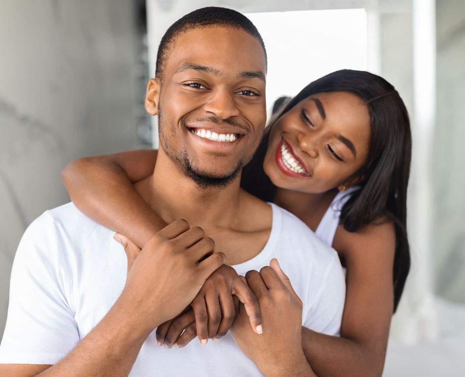 A woman is hugging a man from behind and smiling.