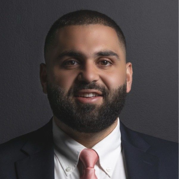 A man in a suit and tie is standing in front of a blue background.