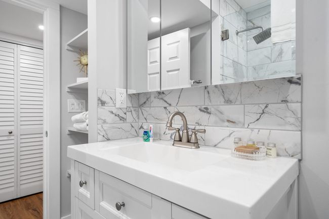 Modern white bathroom vanity with marble backsplash, mirror cabinet, and shower enclosure
