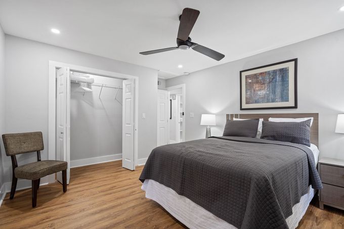 Modern bedroom with gray bed, ceiling fan, chair, open closet, and framed art on the wall