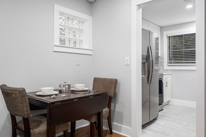 Small dining area beside a bright kitchen with stainless refrigerator and white cabinets