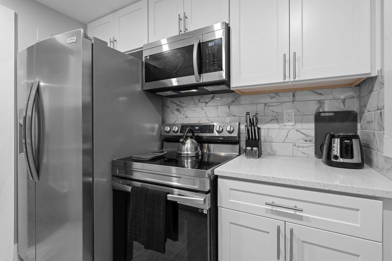 Modern kitchen with stainless steel appliances, white cabinets, stove, microwave, refrigerator, and toaster.