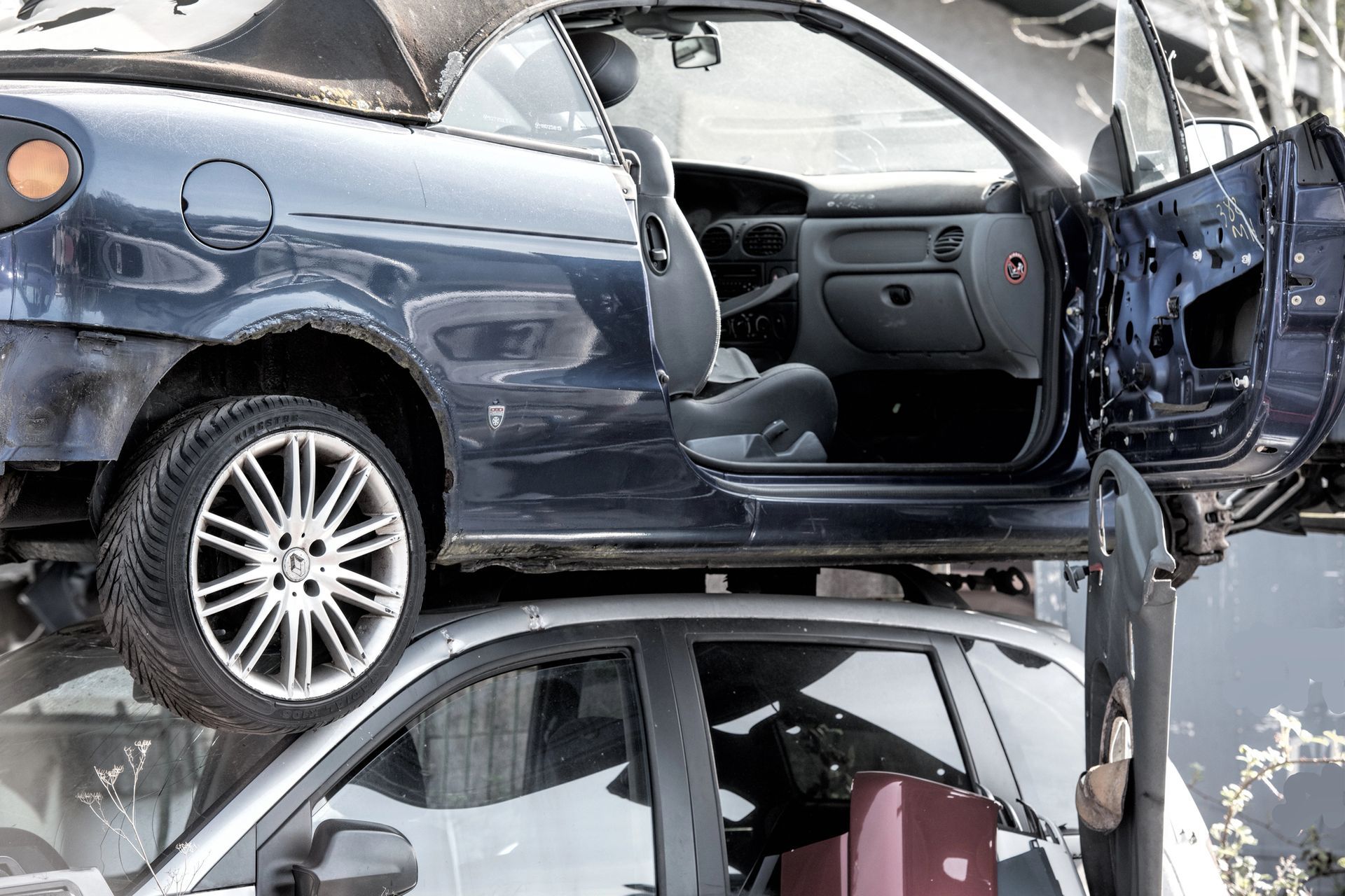 In un deposito di rottami, un'auto blu scuro è impilata sopra un'auto argentata.