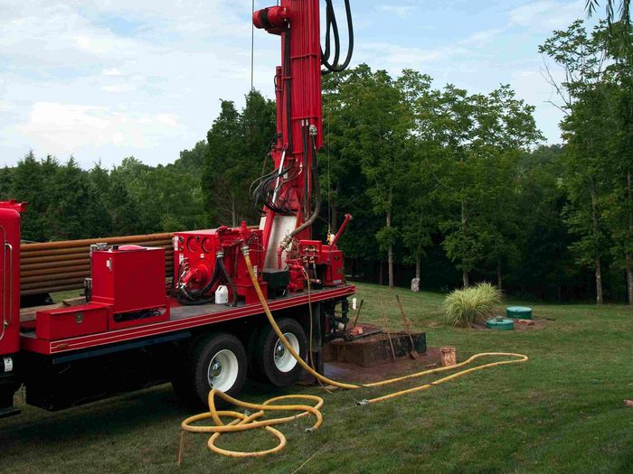 Person in hard hat and gloves lowers bucket into deep, earthen well. Rope attached above in Fayetteville, NC.