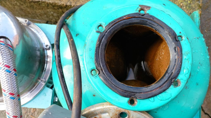 Open end of a teal water pump, showing a corroded interior and black rubber seal.