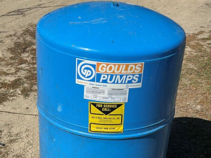 A blue Goulds Pumps pressure tank for a well system, sitting outdoors on a dirt surface.