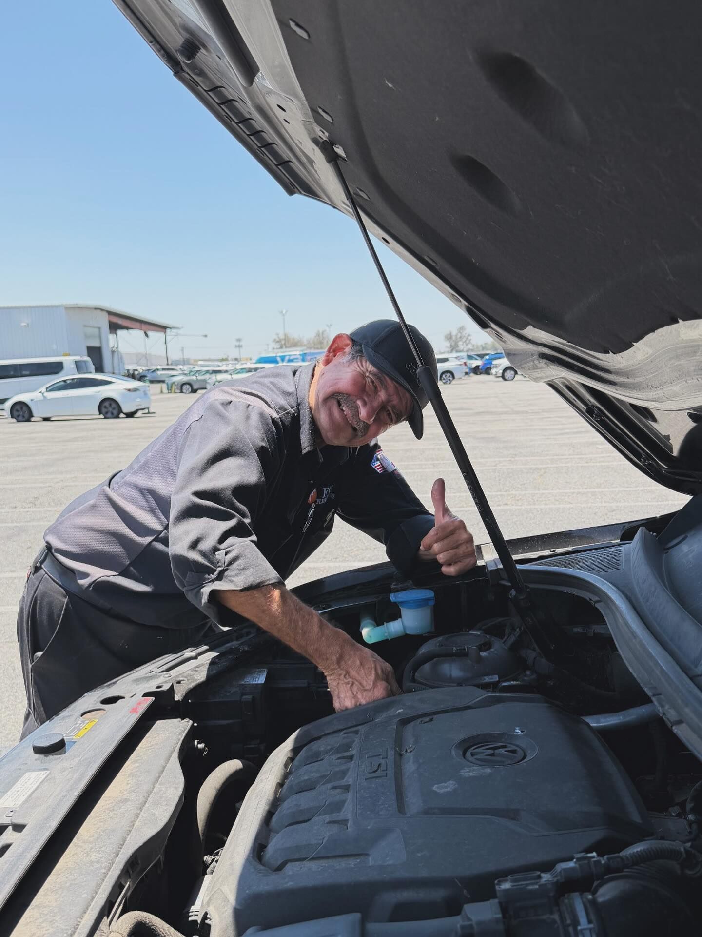 Mechanic checking a car engine under an open hood in a parking lot