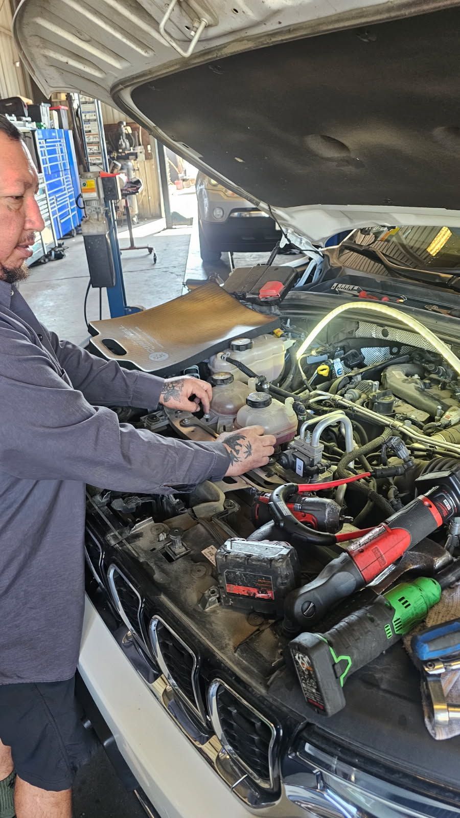 Mechanic working on car engine with tools and open hood in a garage