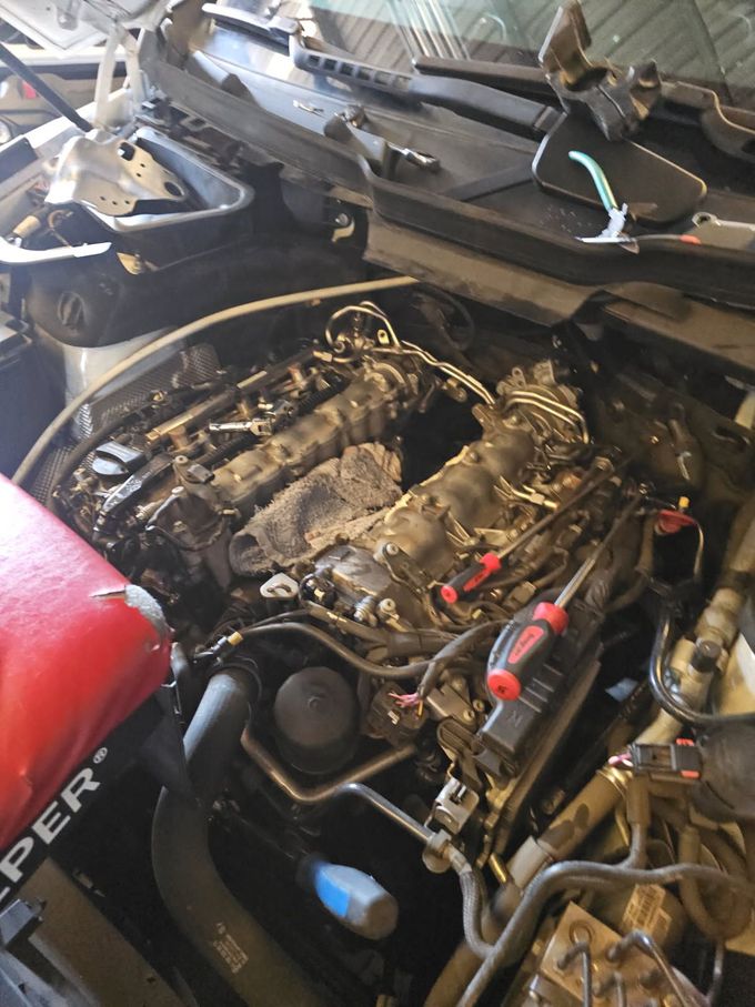 Mechanic tightening an engine cover next to a yellow oil filter in a car engine bay