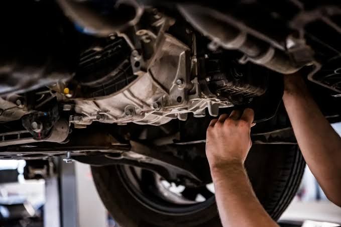 Mechanic working under a car, inspecting the undercarriage in a repair shop