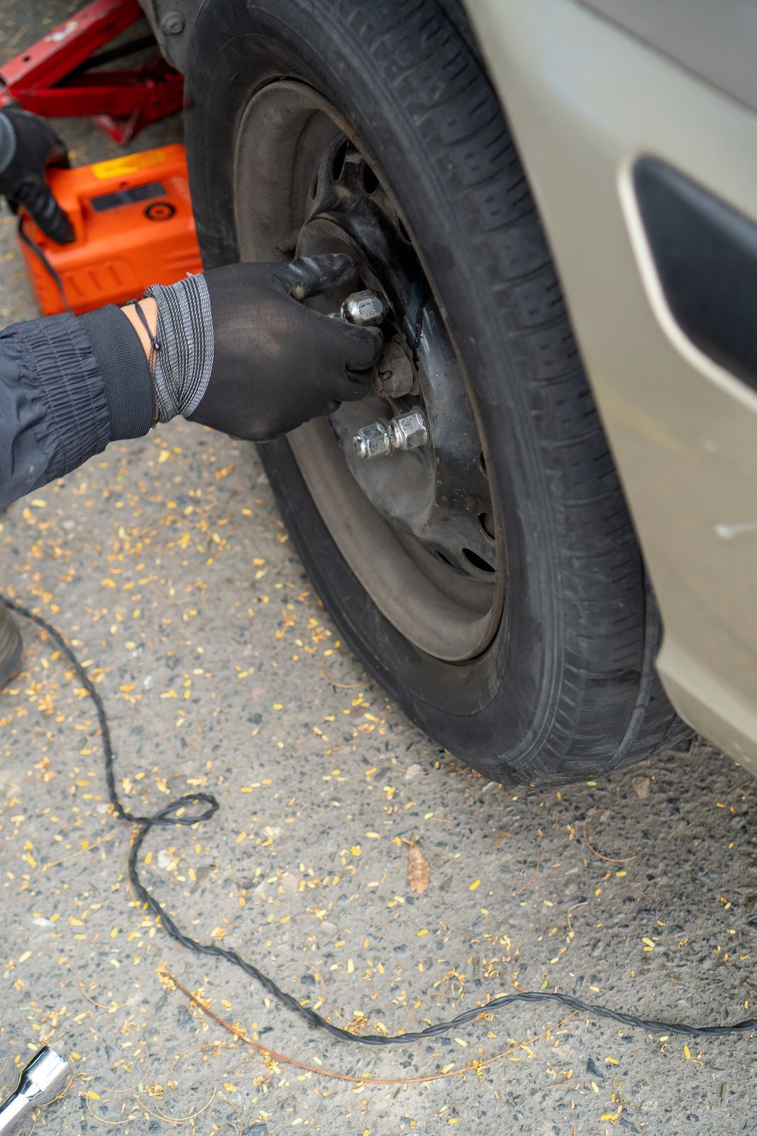 Gloved hands using a tire tool to remove a car wheel on a roadside.