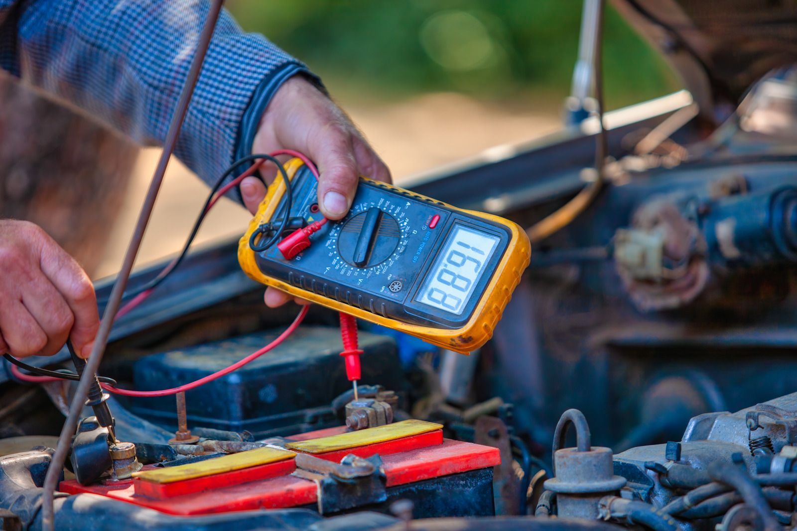 Technician using a multimeter to test car battery wires in an engine bay