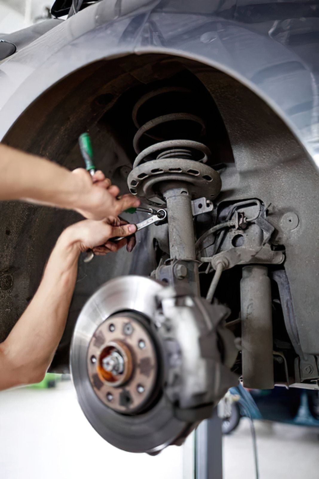 Mechanic repairing a car’s front suspension and brake assembly in a workshop