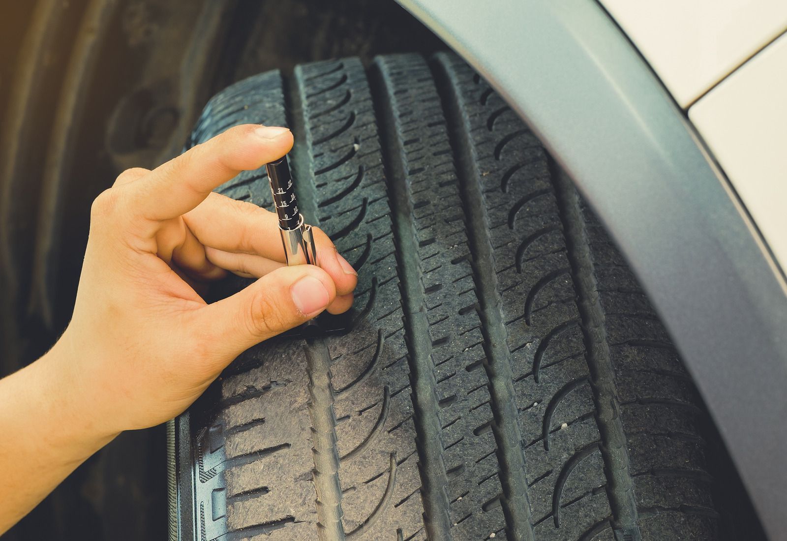 Hand checking tire tread with a gauge on a car wheel