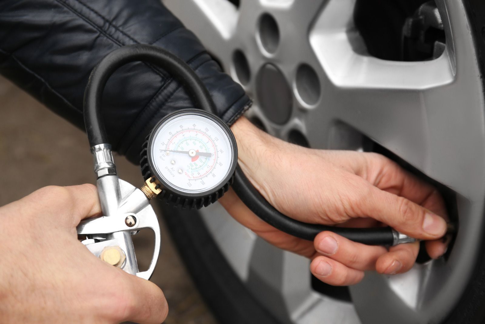 Air pressure gauge and hose being used to check a car tire near a wheel