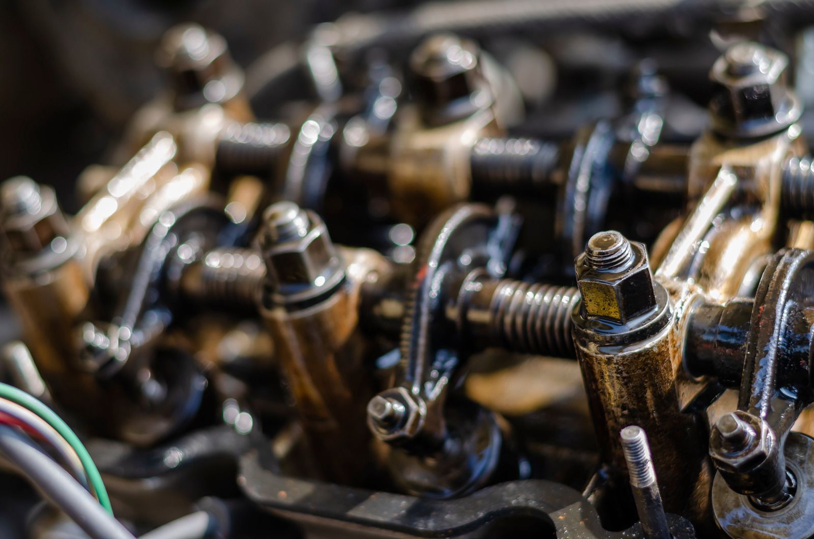Close-up of metal engine rocker arms and bolts with oil-stained parts and wiring.