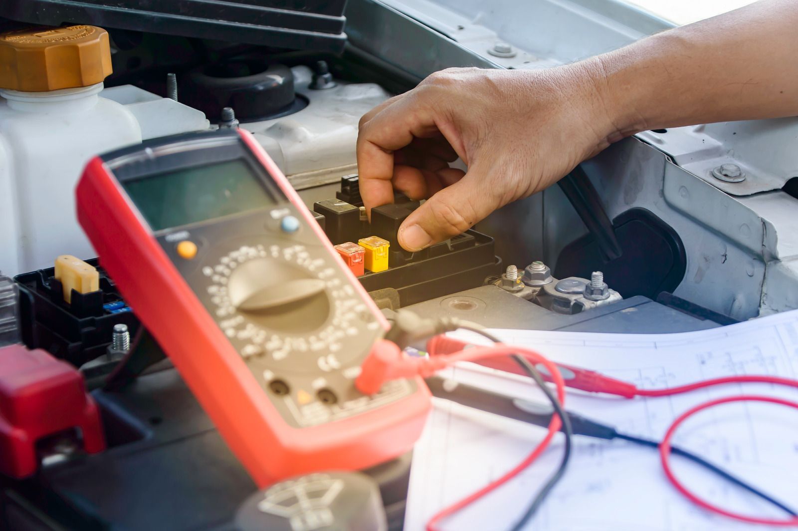 Hand using a multimeter to test a car battery in an engine bay