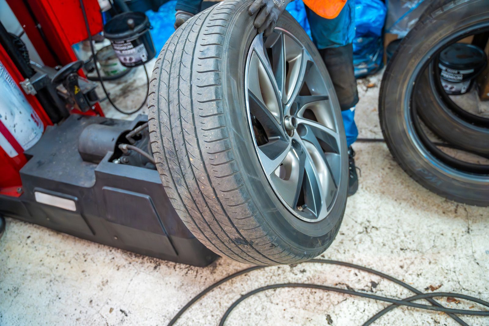 Car tire mounted on a balancing machine in an auto repair shop, with tools and equipment nearby.