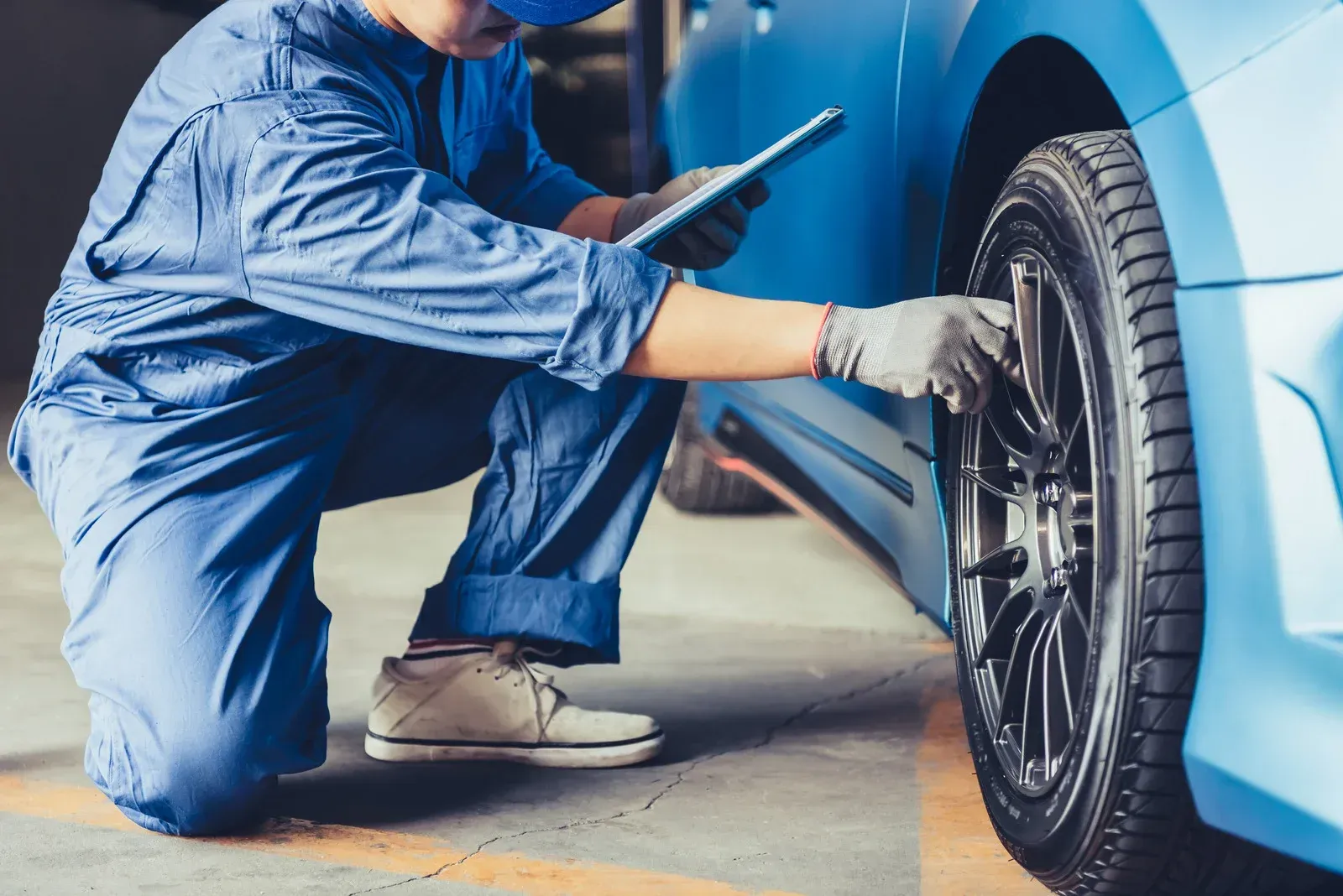 Mechanic in blue coveralls checking a car tire with a tablet in a garage