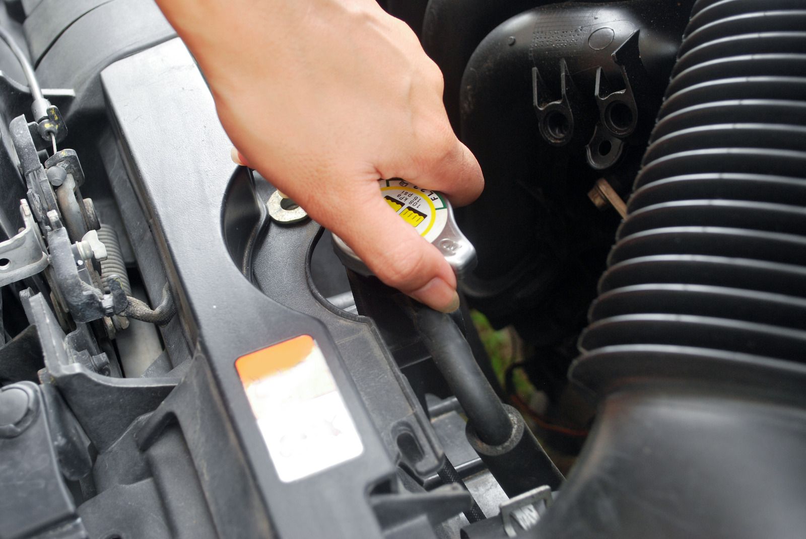 Hand adding coolant to a car engine reservoir under the hood