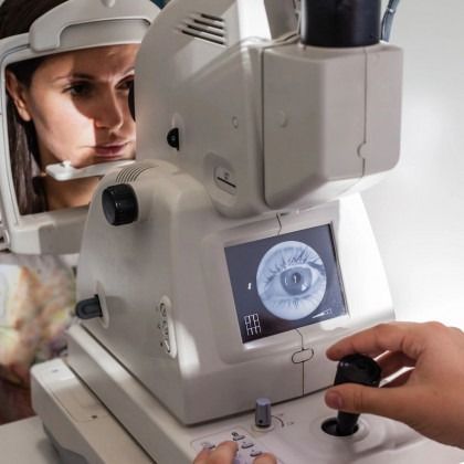 Eye exam in progress as a clinician adjusts a medical imaging device with a patient seated beside it