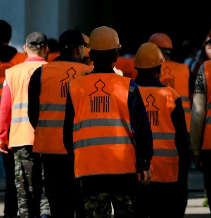Operai con giubbotti di sicurezza arancioni e caschi protettivi in ​​piedi insieme all'aperto.