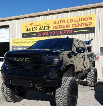Black lifted GMC truck parked in front of an auto collision repair center.