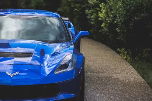 Blue sports car parked on a narrow road beside dense green trees