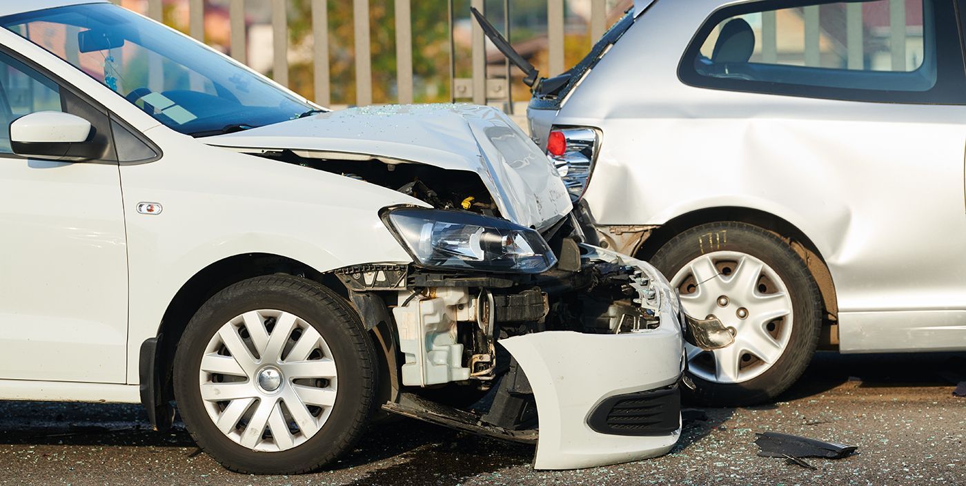 A white car with a crushed hood sits next to a damaged silver car after a traffic accident on a road.