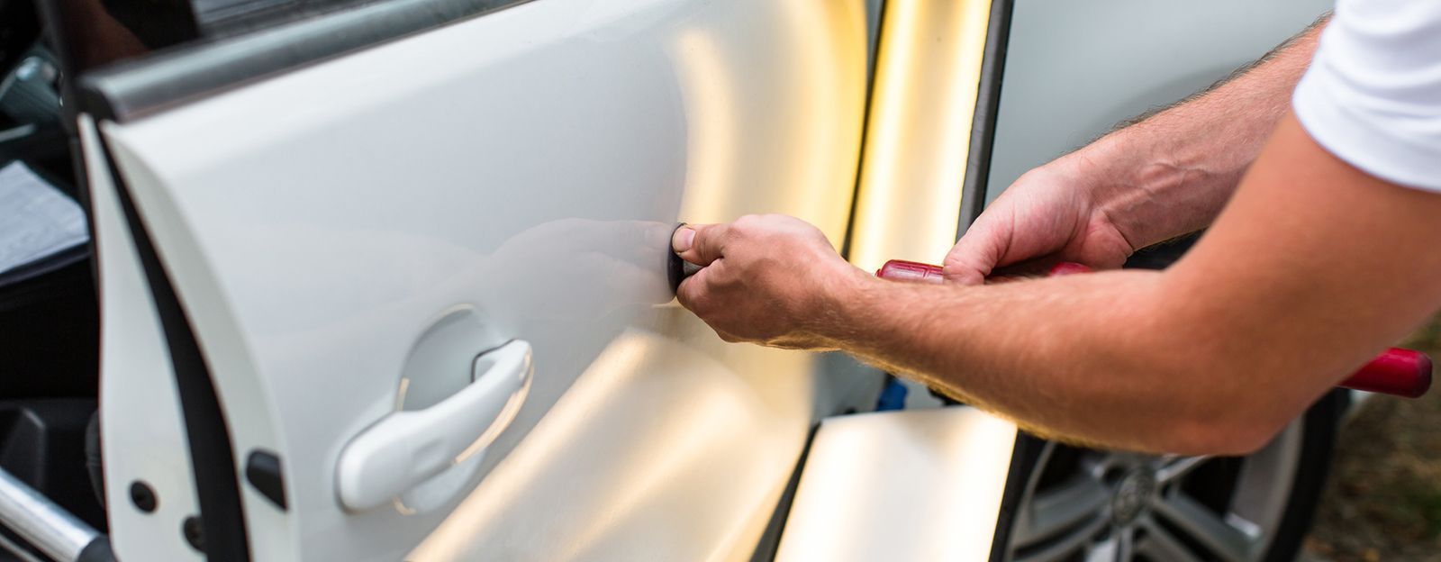 A man is repairing a car door with a hammer.