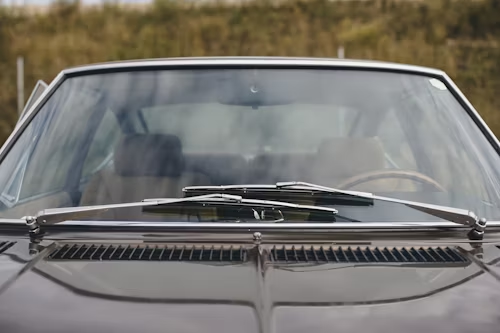 Close-up of a dark car's front, featuring windshield wipers, glass, and vents.