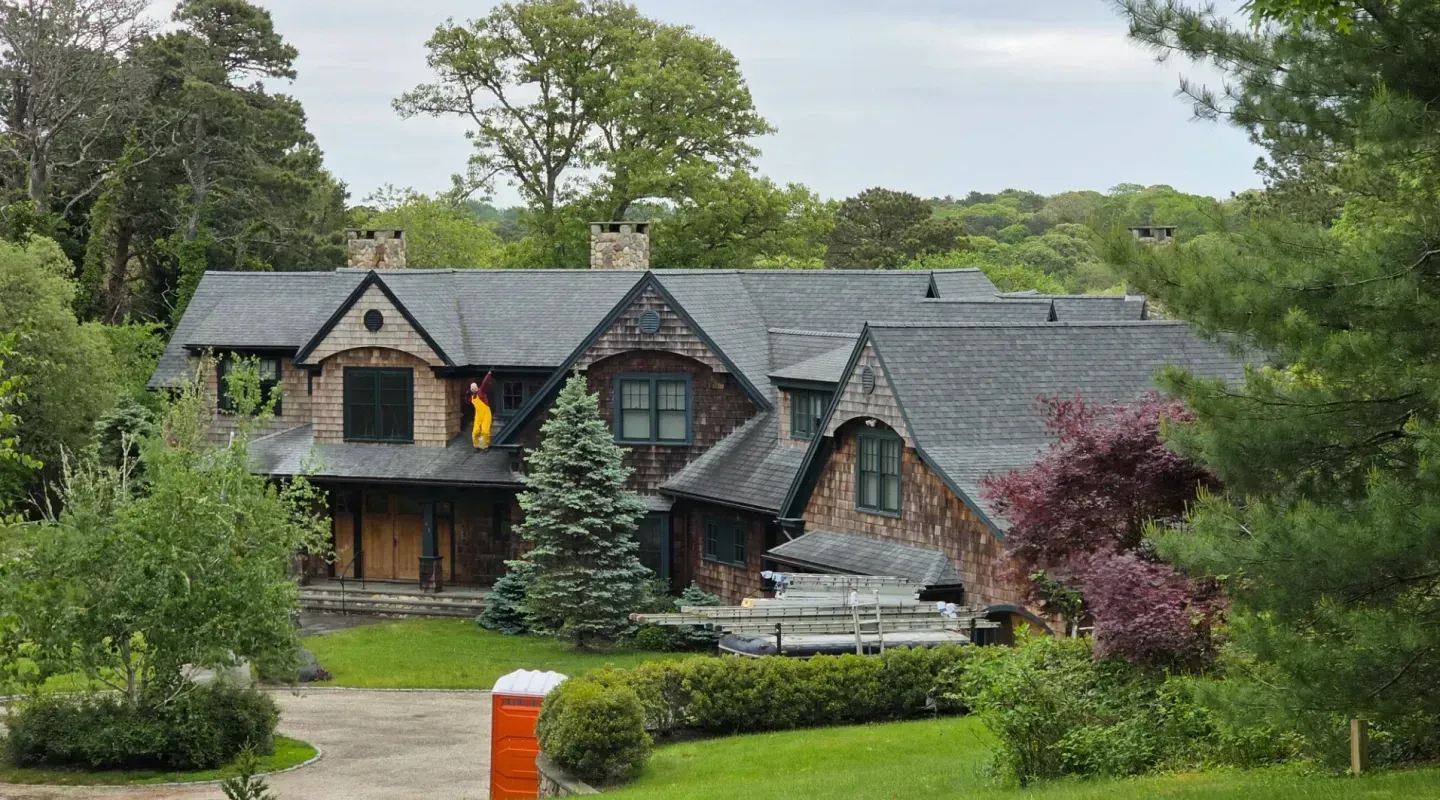 Large stone and timber house with a gabled roof, set amid trees and a manicured lawn