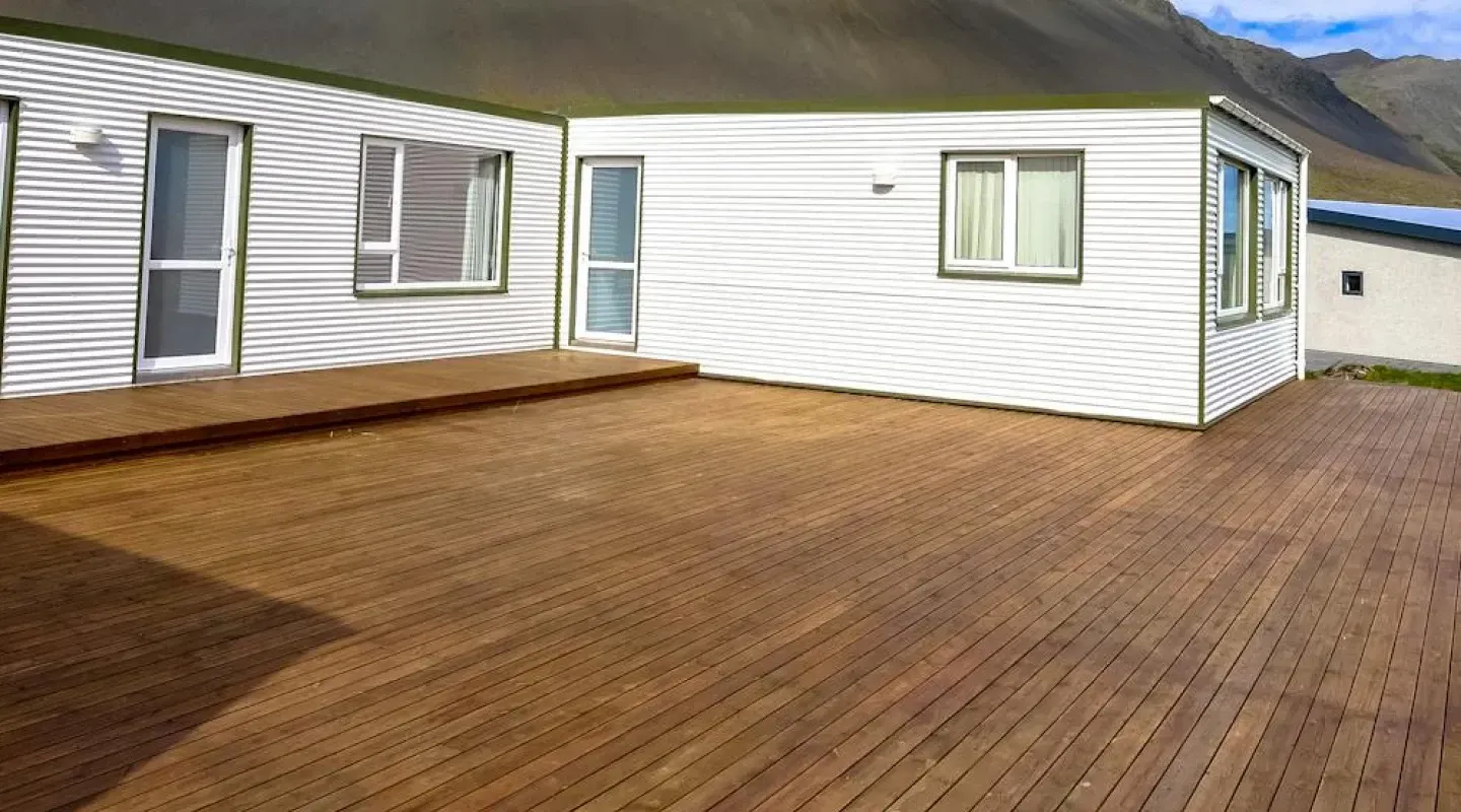 Large wooden deck beside a white house with sliding glass doors and mountain views