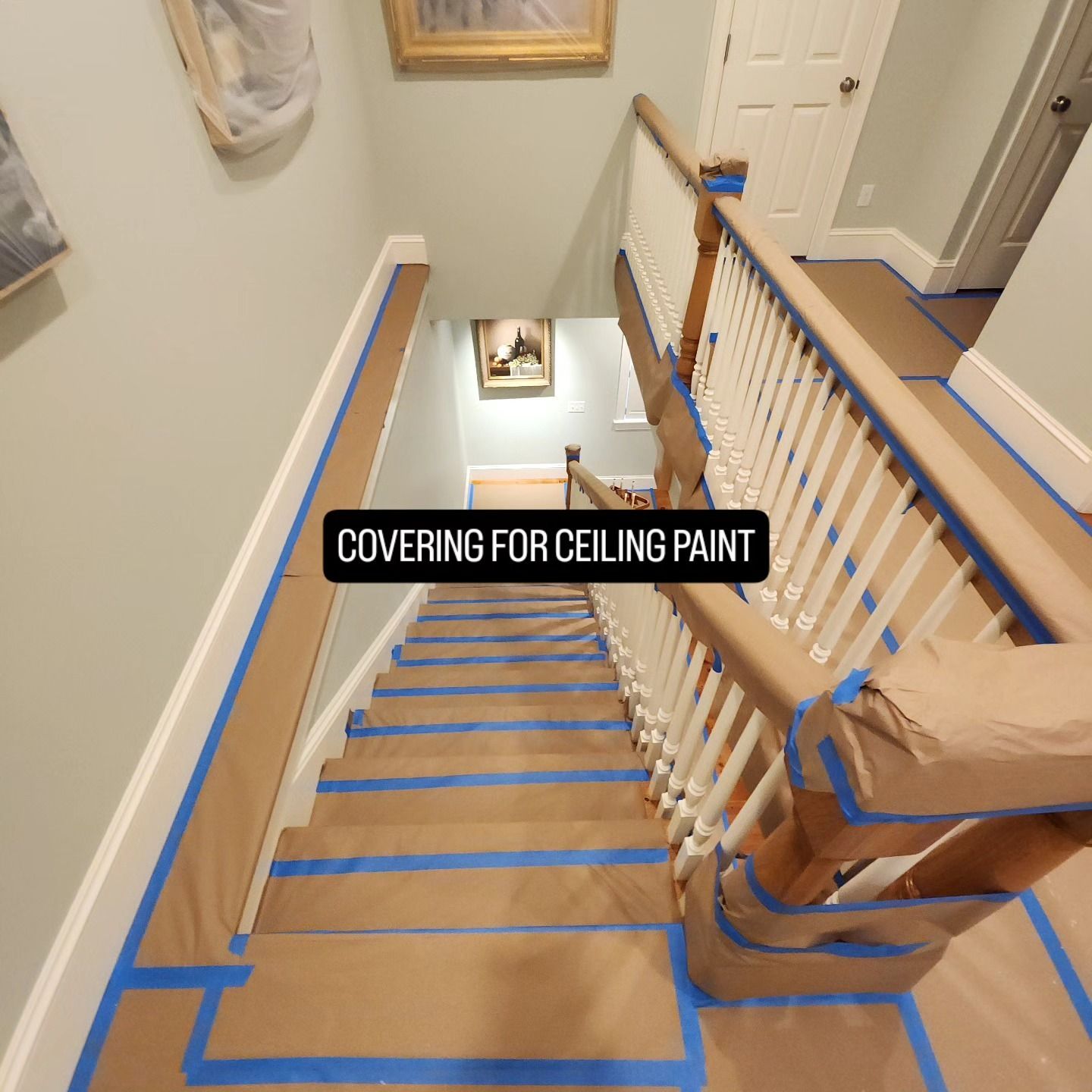Staircase under renovation with blue tape covering floor and railings for ceiling paint.