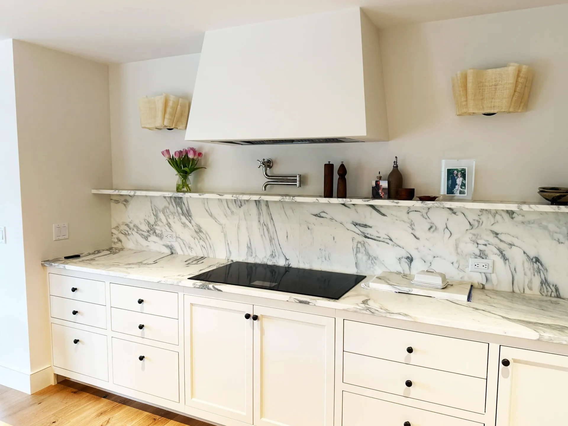 Elegant bathroom vanity with marble backsplash, white cabinetry, and wall sconces