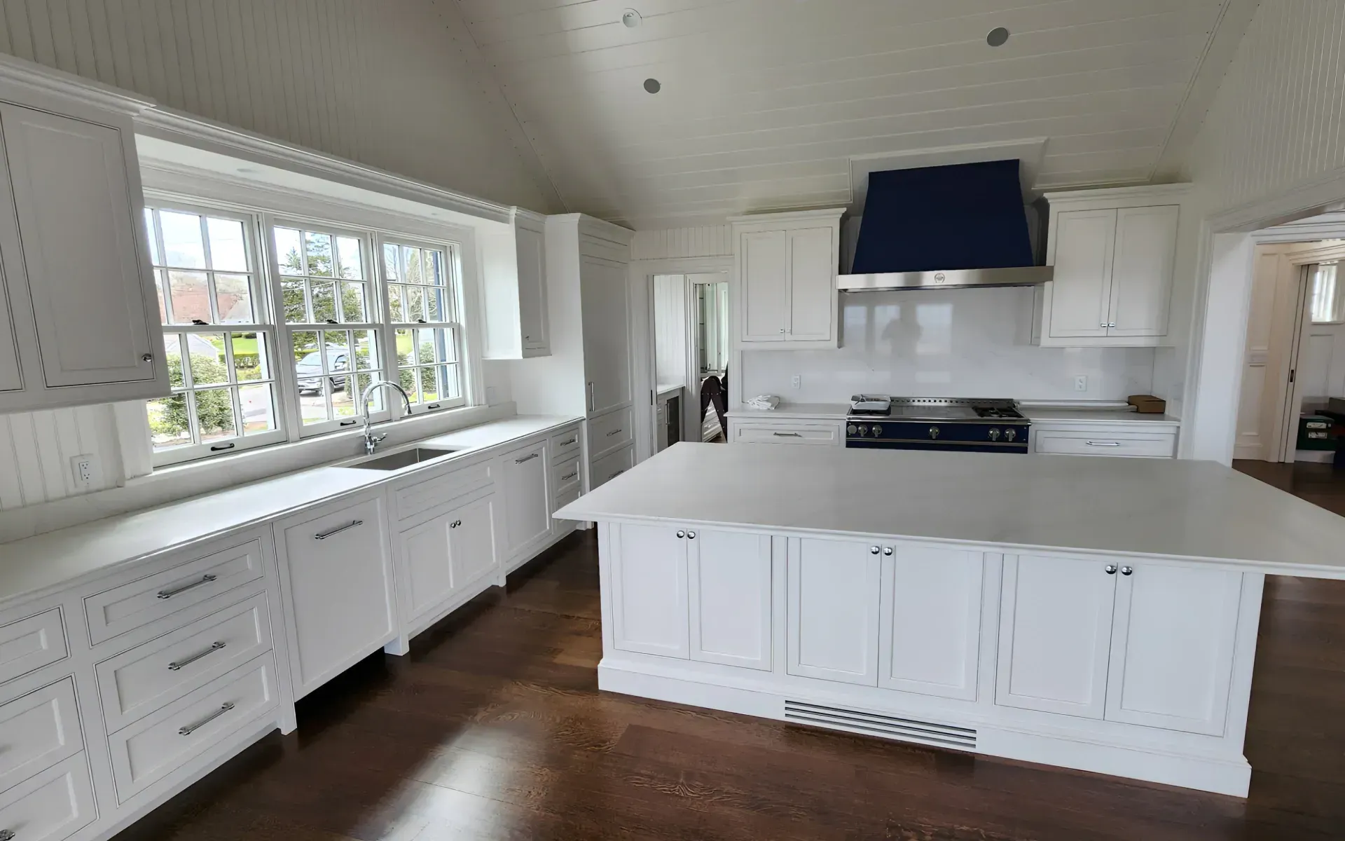 Bright white kitchen with large island, stainless range hood, and long window-lined counter.