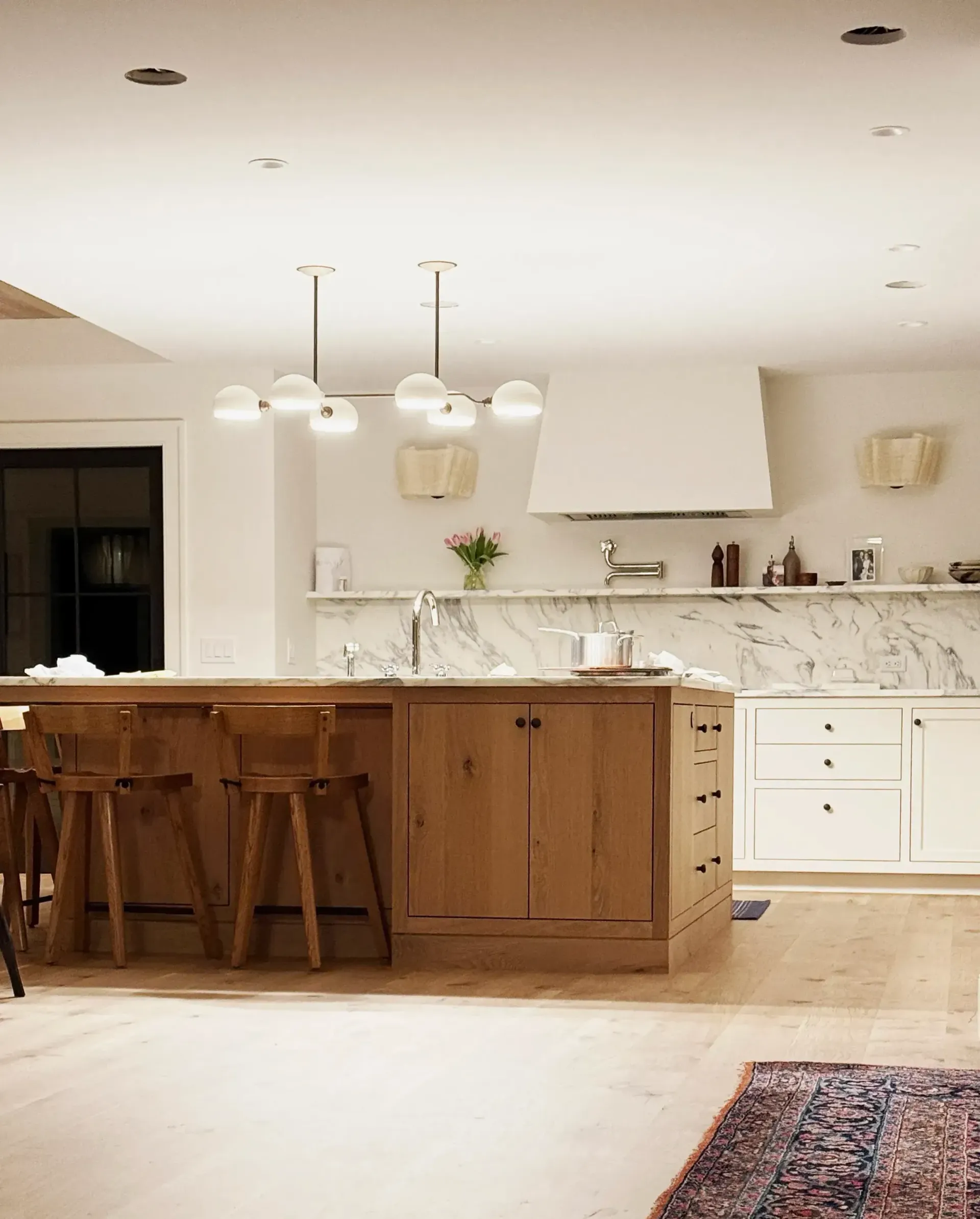 Modern kitchen with wood island, white cabinets, pendant lights, and a patterned rug