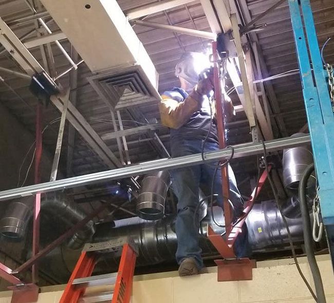 A man wearing a welding mask is working on a pipe