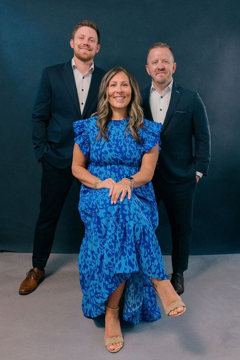 Three people posing in formal attire against a dark backdrop