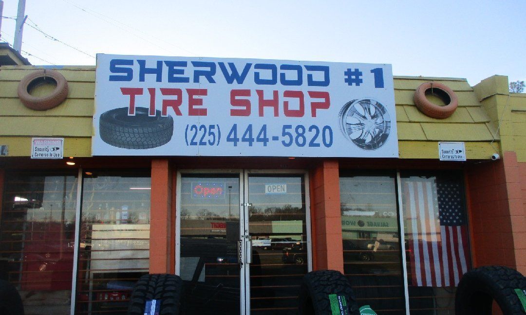 Sherwood #1 Tire Shop storefront with a sign, phone number, and American flag. Orange building, tires displayed outside.