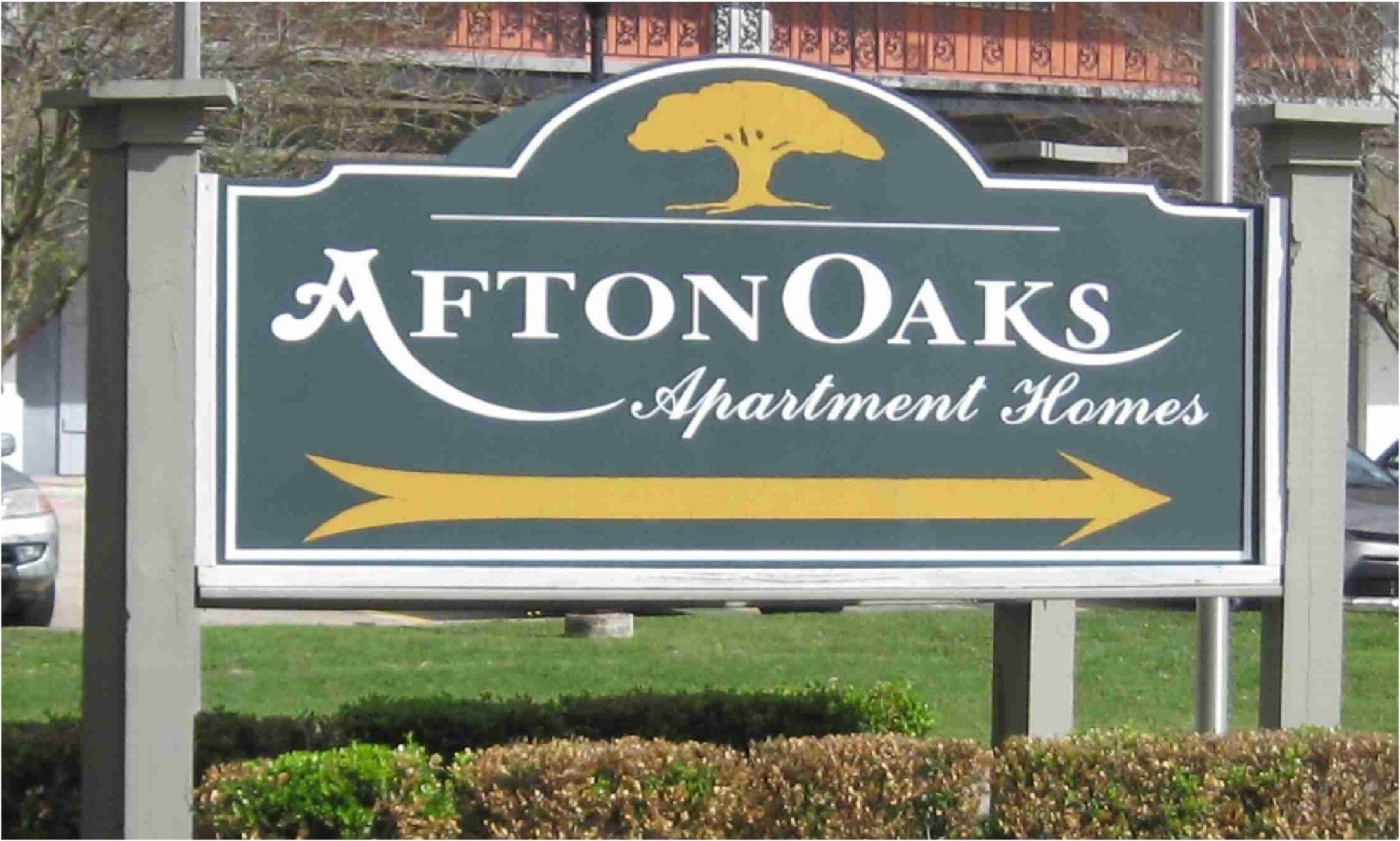 Afton Oaks Apartment Homes sign in green, white, and gold with an arrow pointing right.