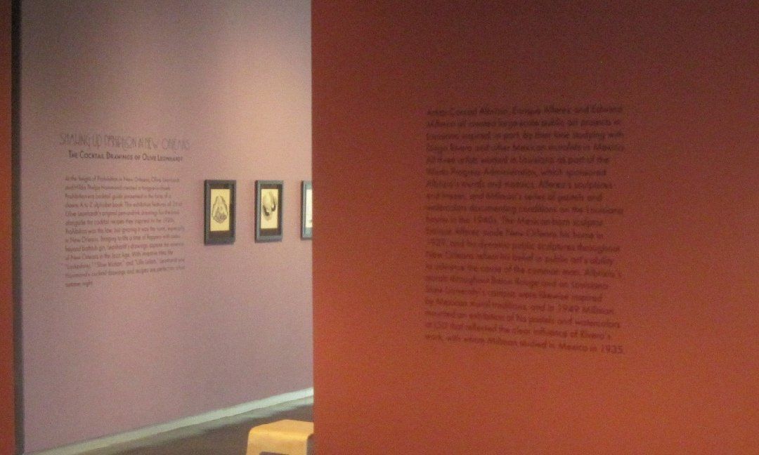 Interior view of a museum exhibit with reddish-brown and purple walls. Text is visible on both walls, and small framed pictures hang on the purple wall.