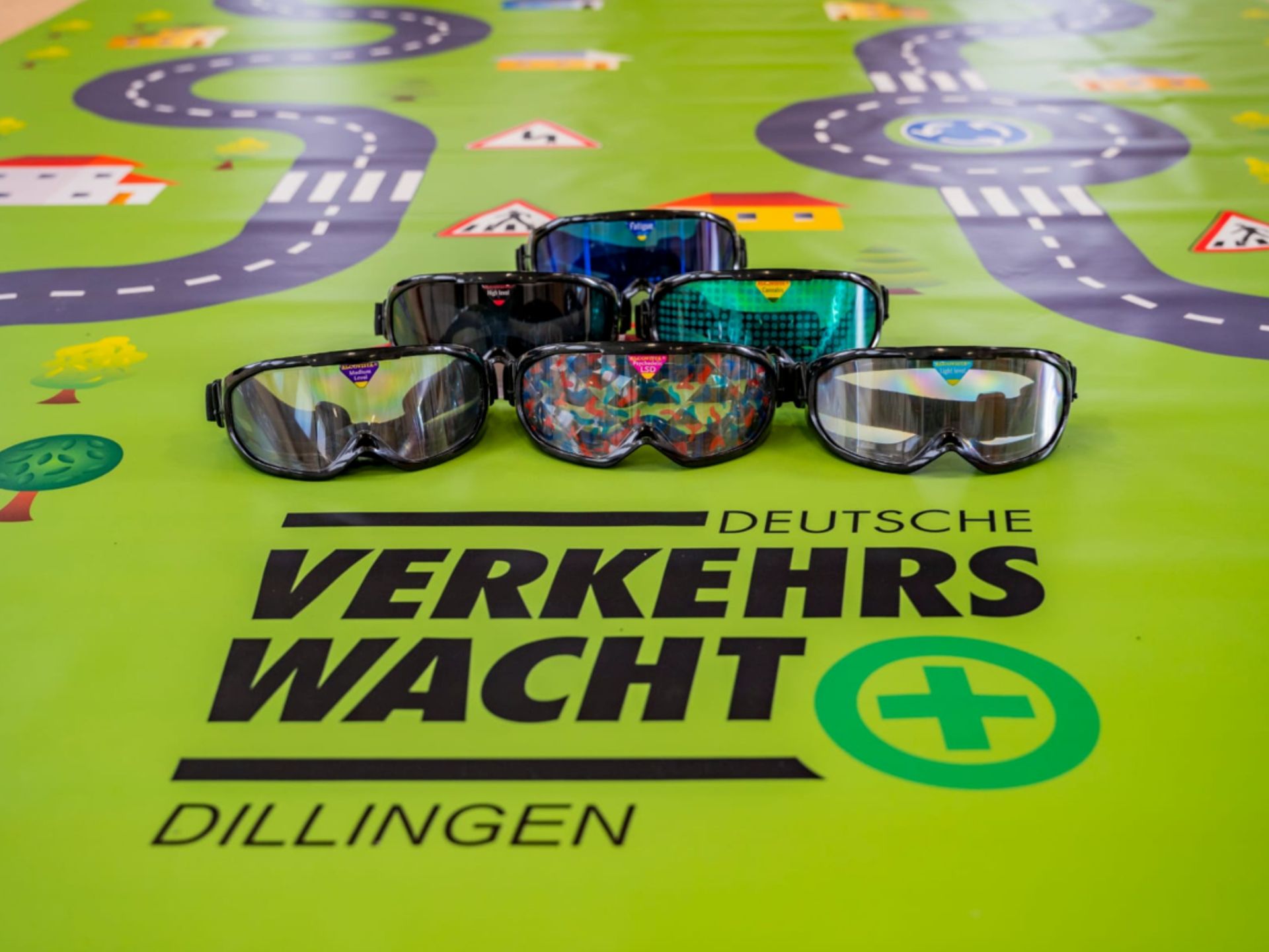 Ein paar Schutzbrillen liegen auf einer grünen Matte mit der Aufschrift „Verkehrswacht“.