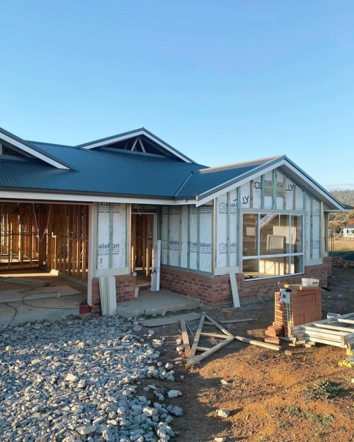 A House is Being Built With a Blue Roof and a Lot of Rocks in Front of It  — Trussted Frames & Trusses In Taminda, NSW