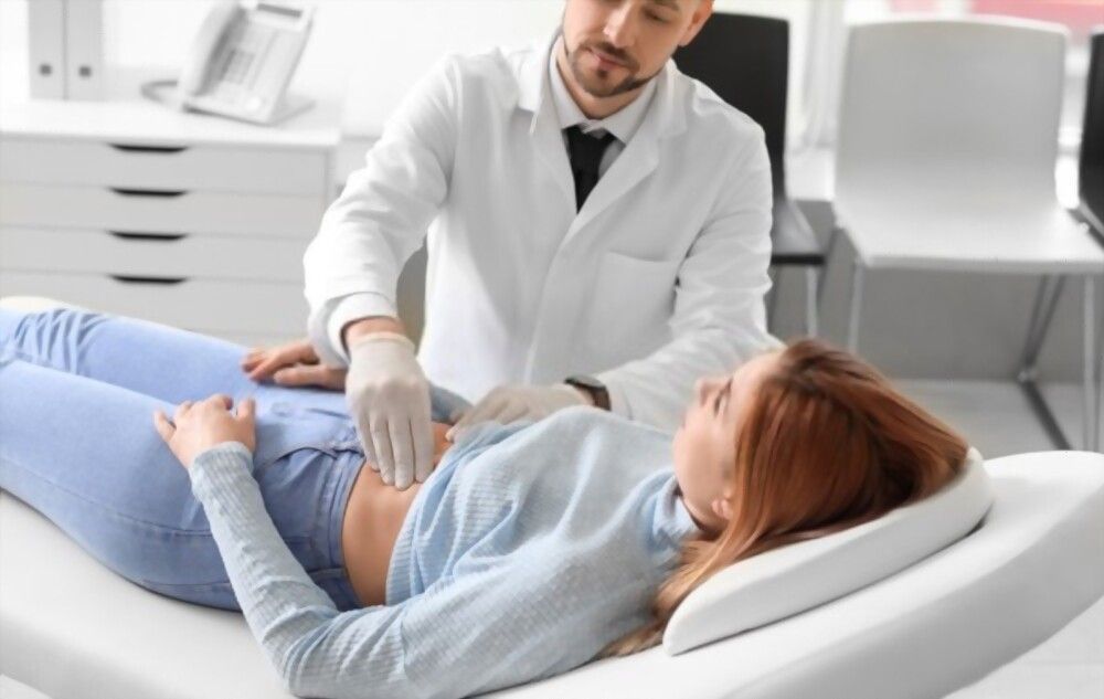 A woman is laying on a bed while a doctor examines her stomach.