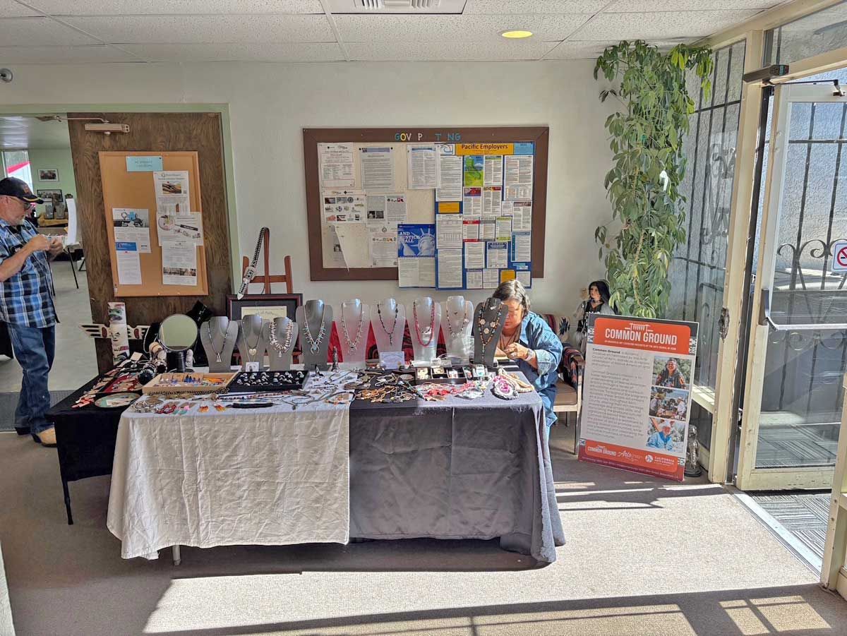 A vendor table with jewelry displays sits in an indoor room with a bulletin board and a person standing nearby.