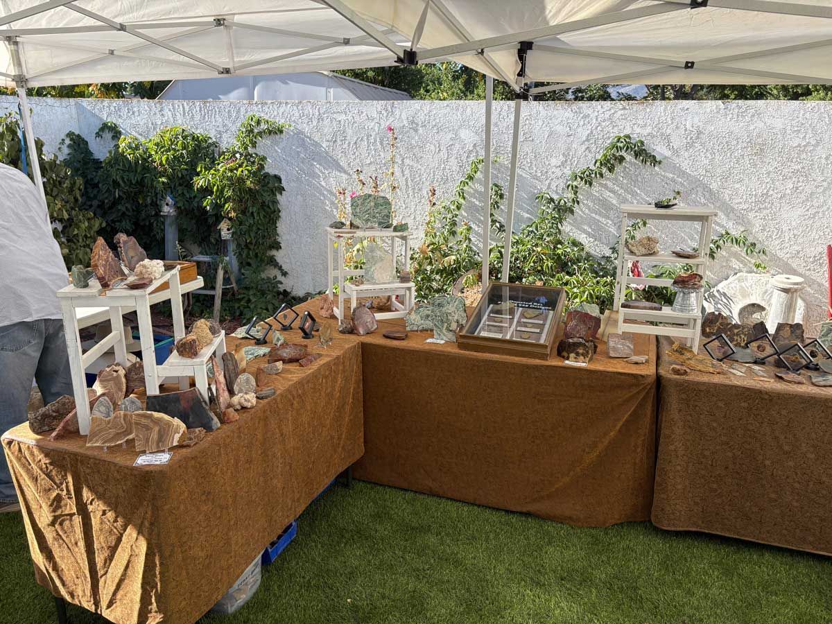 A vendor's booth at an outdoor market displays various crystals and rocks on tables covered in brown textured cloths.