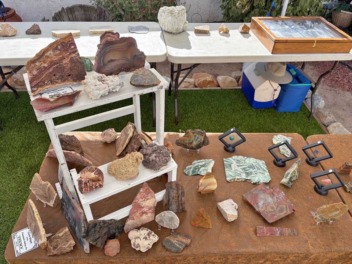 Rocks and minerals displayed on a white tiered shelf and a brown table at an outdoor market.