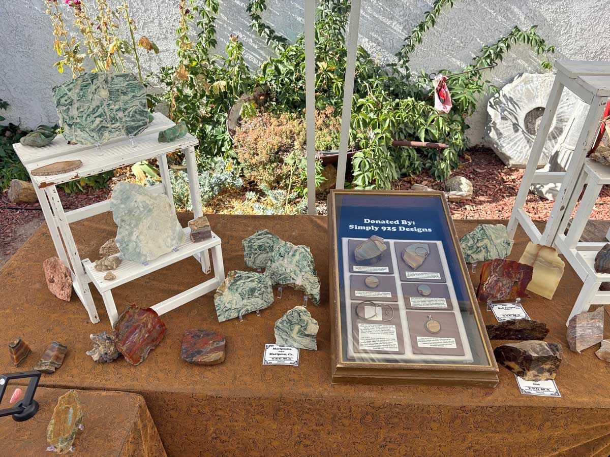 A display of various raw mineral specimens and polished rocks arranged on a brown table outdoors.